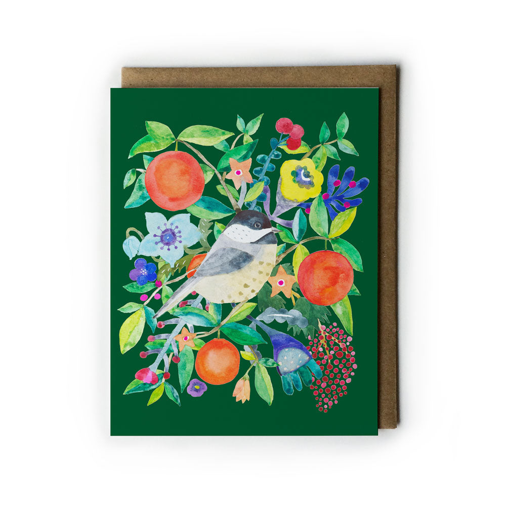 Watercolor holiday greeting card featuring a chickadee bird surrounded by vibrant orange fruits, colorful flowers, and festive foliage on a deep green background, paired with a kraft paper envelope