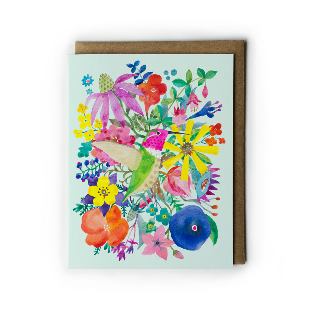 Colorful watercolor greeting card featuring a vibrant hummingbird surrounded by diverse flowers and foliage on a light blue background, paired with a kraft envelope