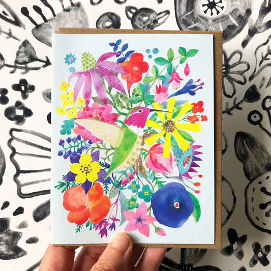 Colorful watercolor greeting card featuring a vibrant hummingbird surrounded by diverse floral elements, including purple coneflowers, yellow daisies, red poppies, and blue blossoms, displayed on a white background with a kraft envelope