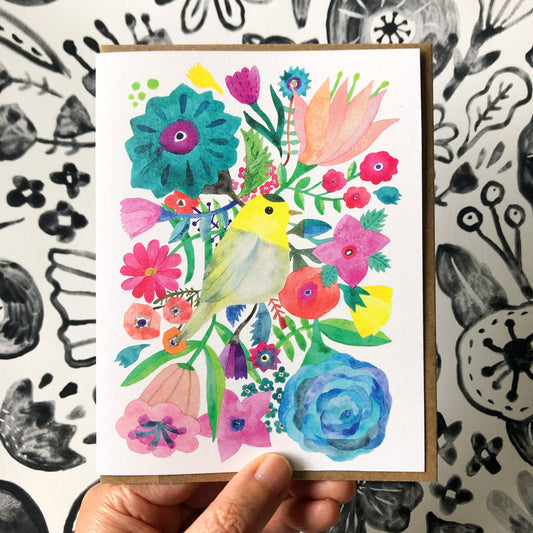 Colorful watercolor greeting card featuring a yellow warbler surrounded by vibrant flowers and foliage, hand-held against a black and white patterned background