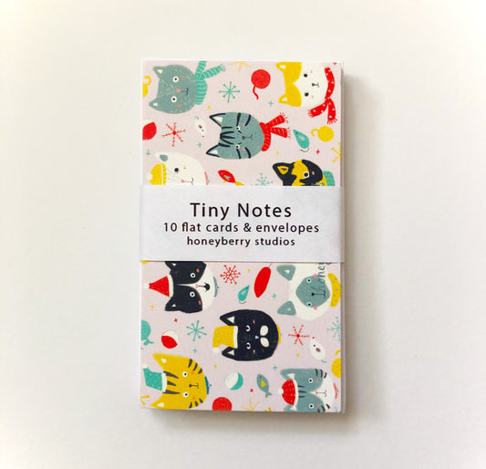 Colorful set of tiny notes featuring whimsical winter cat designs, snowflakes, and festive elements on a light background, packaged with a white band labeled "Tiny Notes" by Honeyberry Studios