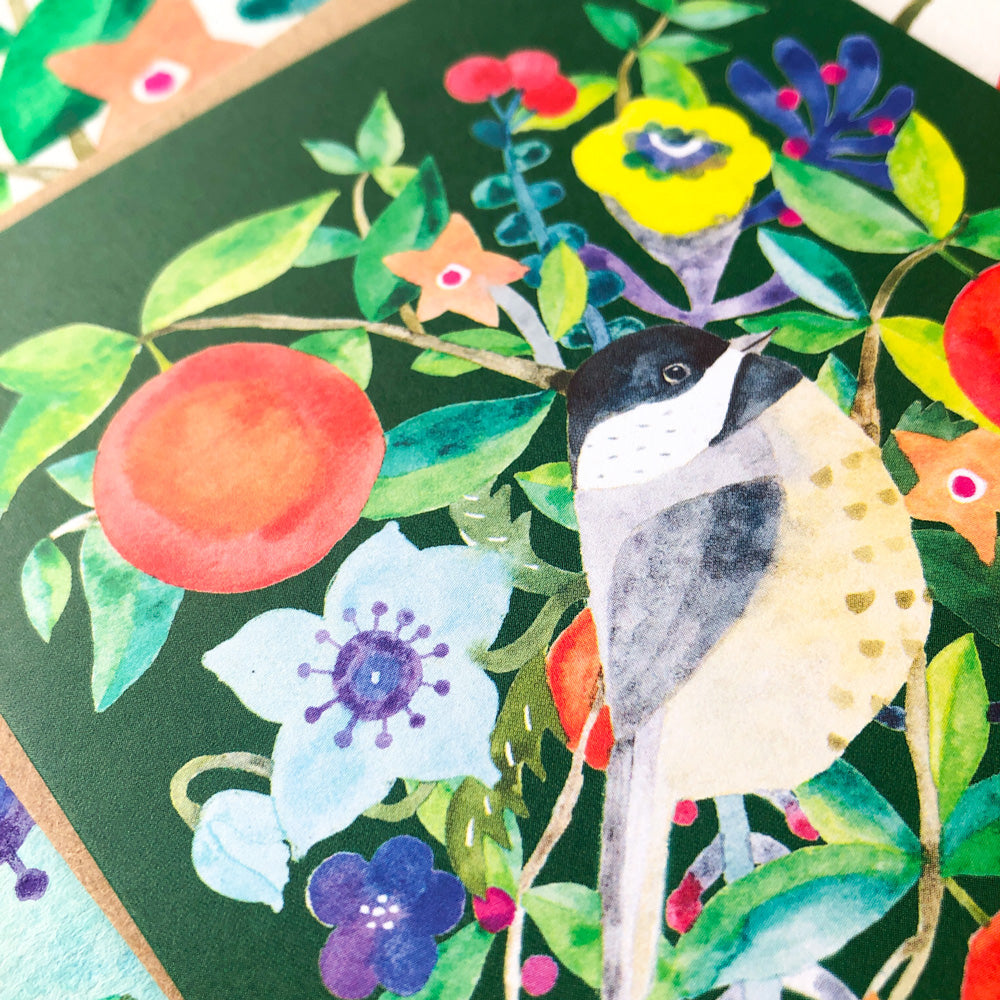 Watercolor holiday greeting card featuring a chickadee perched among vibrant flowers, leaves, and an orange. Colorful botanical elements surround the bird on a dark green background, creating a festive and nature-inspired design.