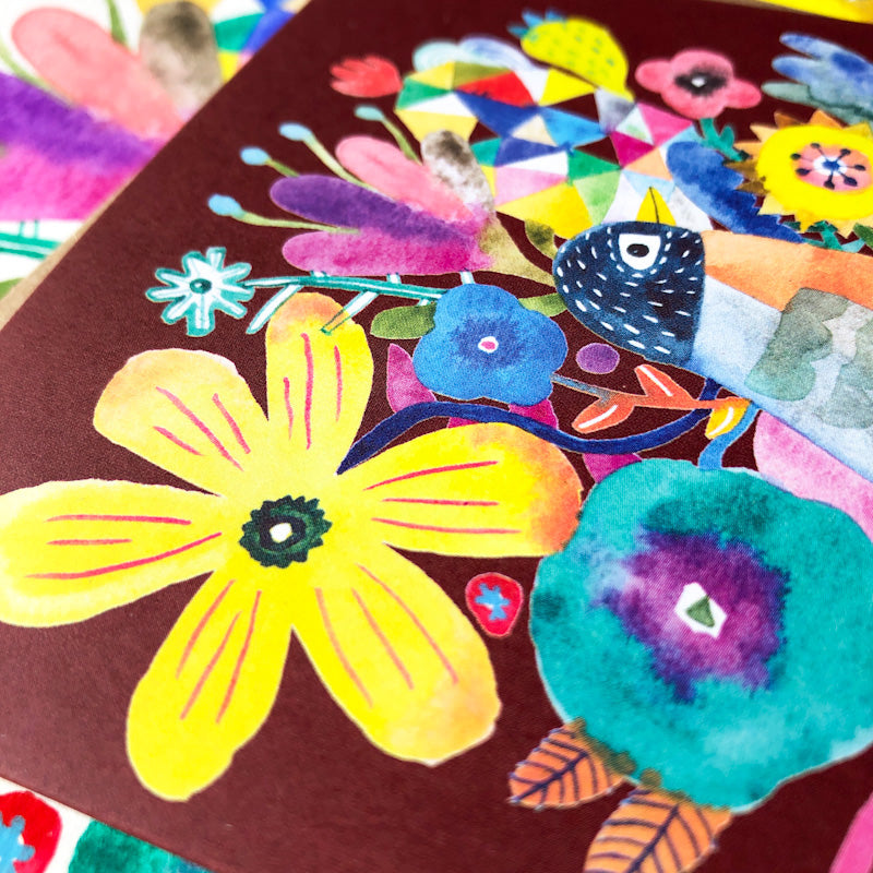 Colorful watercolor greeting card featuring vibrant floral design with yellow, blue, and purple flowers, butterflies, and a stylized bird on a burgundy background. Close-up view showing intricate details and textures of the artistic illustration.
