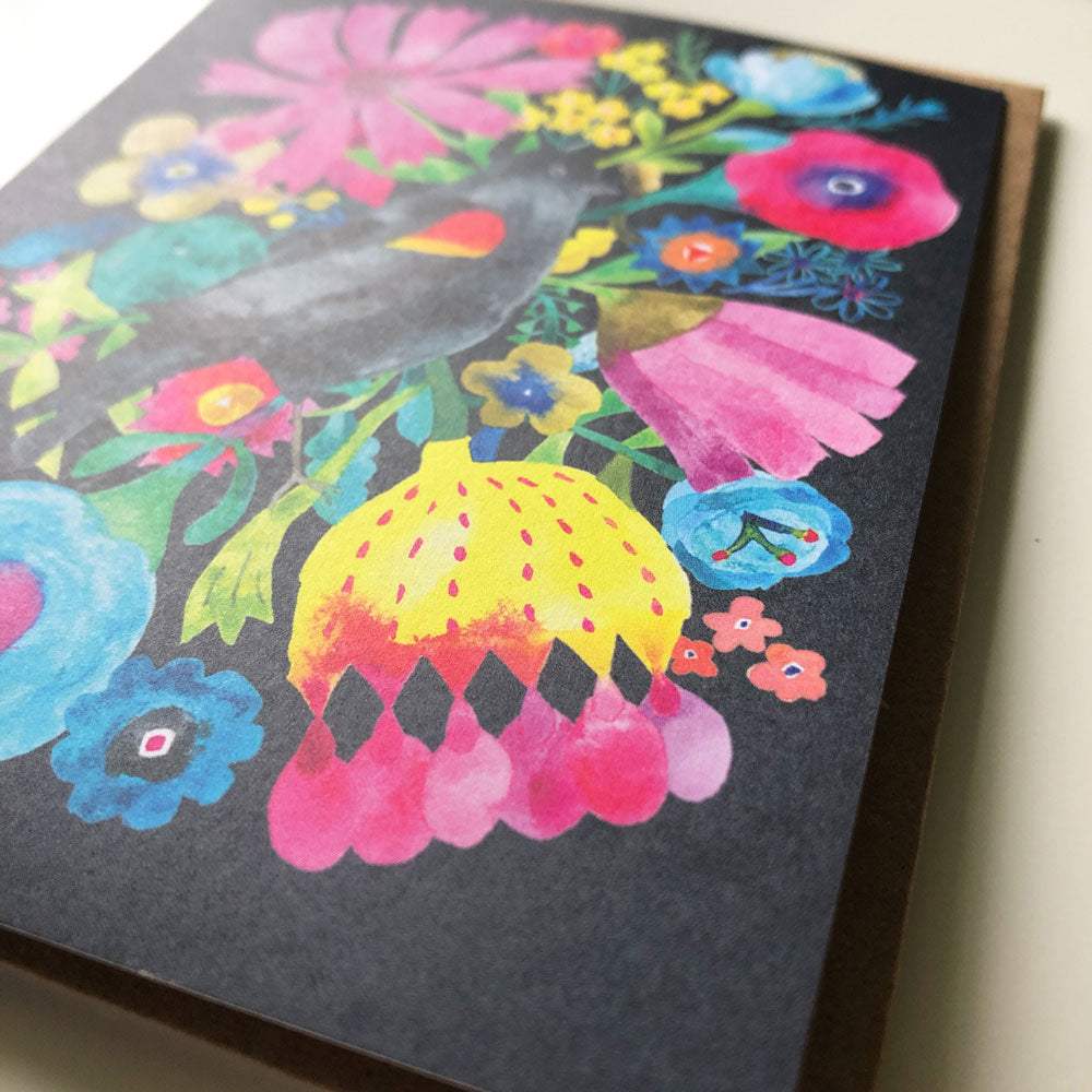 Vibrant watercolor greeting card featuring a blackbird silhouette surrounded by colorful flowers on a dark background, showcasing pink, yellow, blue, and red blooms in a whimsical, folk art style