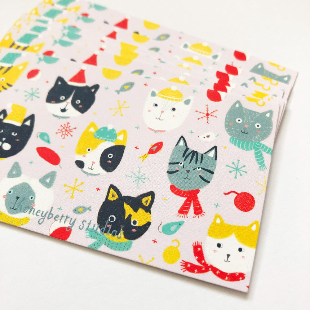 Colorful winter-themed tiny note card featuring adorable cartoon cat faces, snowflakes, and festive elements like Santa hats and scarves on a light background, perfect for holiday greetings and gift tags