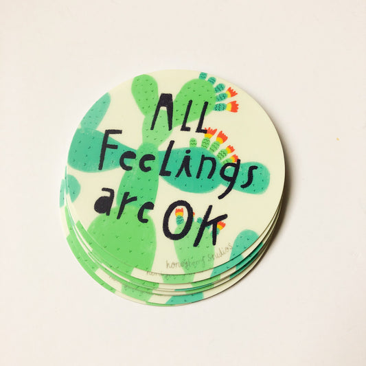 Circular vinyl sticker with green cactus design and hand-lettered text "All Feelings are OK", surrounded by colorful dots, on cream background