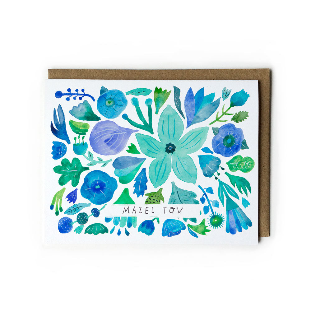 Watercolor greeting card with vibrant blue and green floral design, featuring various stylized flowers and leaves. Text reads "Mazel Tov" in the center. Accompanied by a kraft paper envelope.