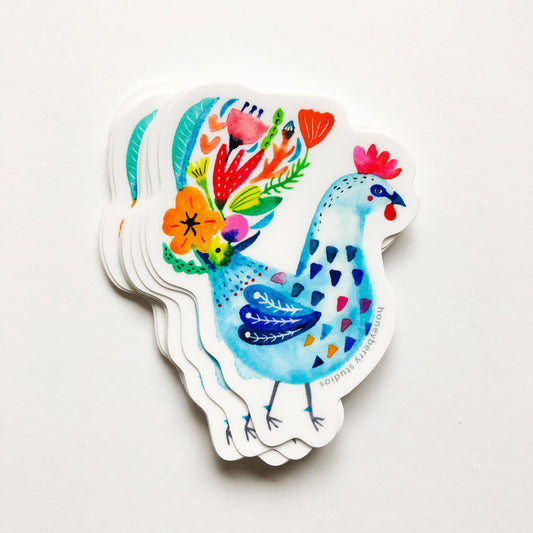 Colorful watercolor-style rooster sticker with vibrant floral tail feathers, featuring blue body, red comb, and decorative patterns, showcasing whimsical folk art design on white background
