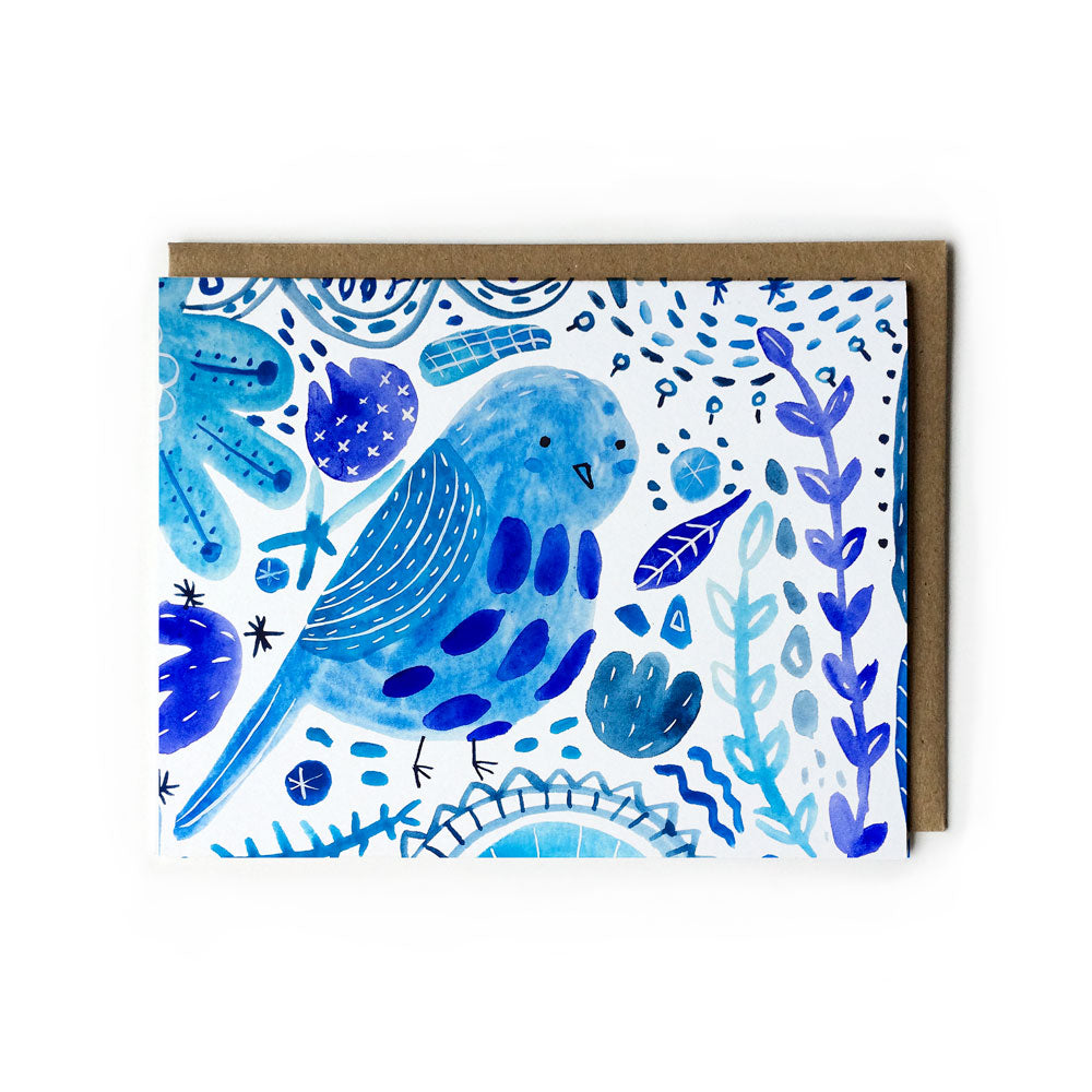 Watercolor illustration of a blue bird surrounded by whimsical floral patterns and abstract shapes on a white notecard with a brown envelope