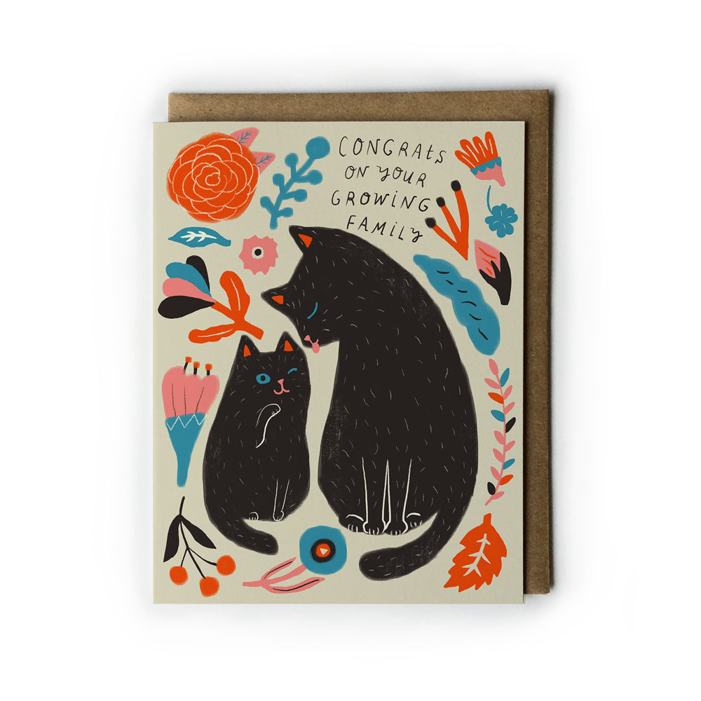Colorful greeting card featuring two black cats surrounded by floral designs, with text "Congrats on your growing family" on cream background, paired with kraft paper envelope