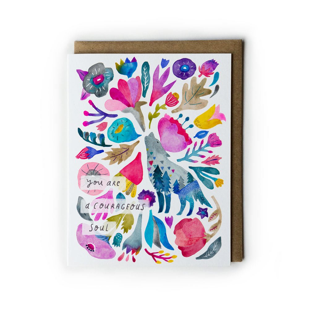 Colorful watercolor greeting card featuring a howling coyote surrounded by vibrant flowers, leaves, and abstract shapes. Text reads "you are a courageous soul". Card shown with matching kraft paper envelope.