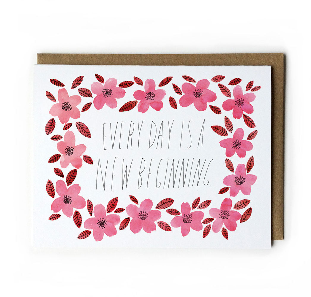 Greeting card with handwritten message "Every day is a new beginning" surrounded by pink watercolor flowers and red leaves, paired with a kraft paper envelope