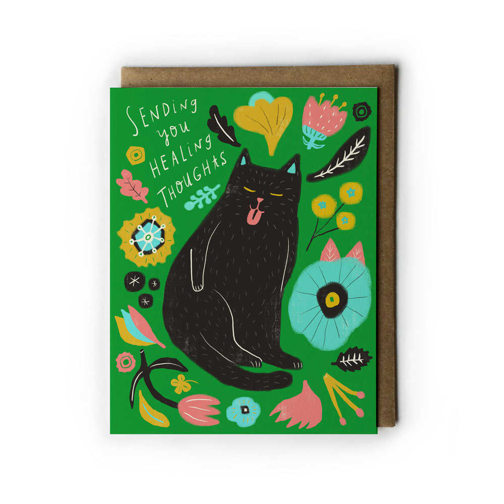 Colorful sympathy card featuring a black cat surrounded by whimsical flowers and leaves on a bright green background, with "Sending you healing thoughts" handwritten text