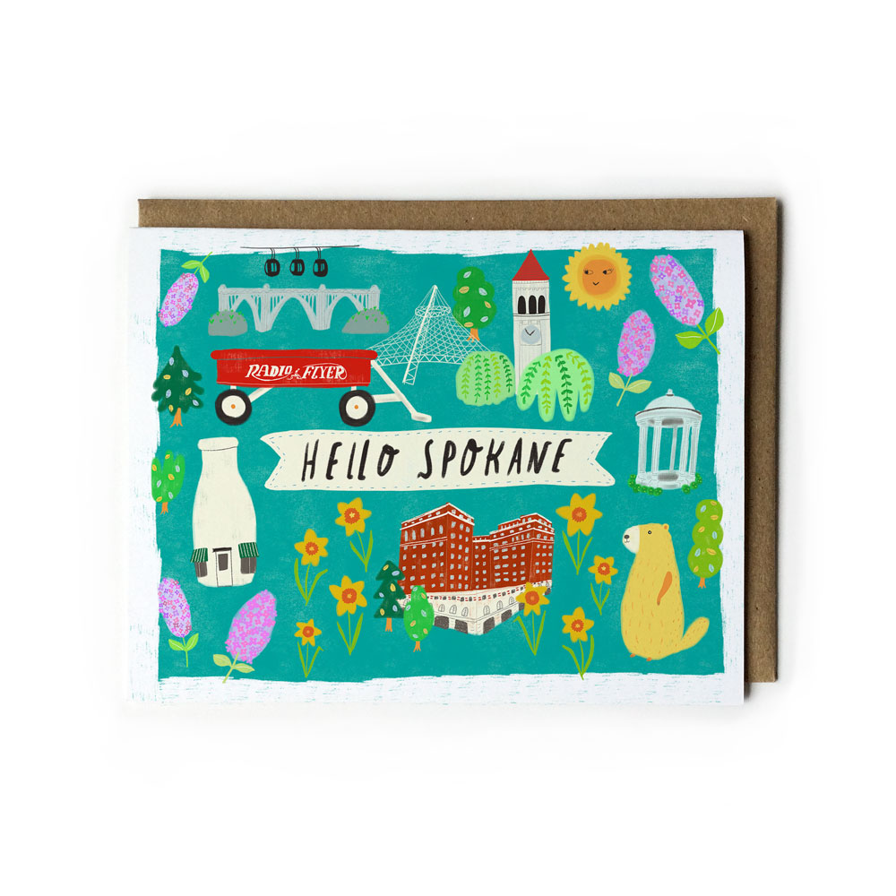 Colorful greeting card featuring Spokane landmarks and symbols including Monroe Bridge, Radio Flyer wagon, clocktower, Davenport Hotel, milk bottle, and marmot, with "Hello Spokane" text on teal background, accompanied by kraft paper envelope.