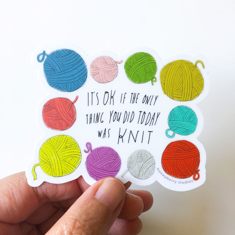 Colorful vinyl sticker featuring yarn balls surrounding text "It's OK if the only thing you did today was knit" held by hand, perfect for knitting enthusiasts