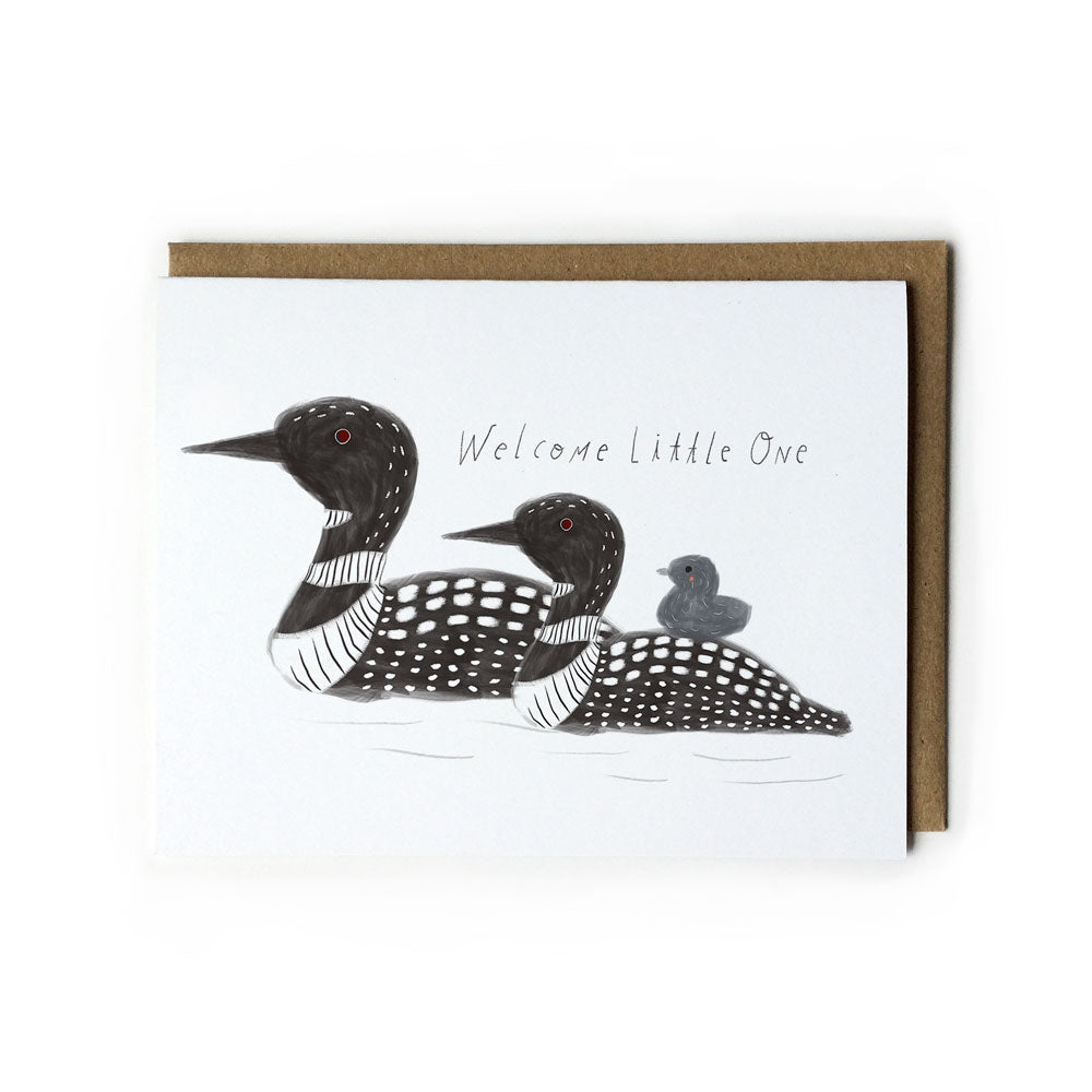 Illustrated greeting card featuring two black and white loons with a baby loon, handwritten text "Welcome Little One", and a kraft paper envelope