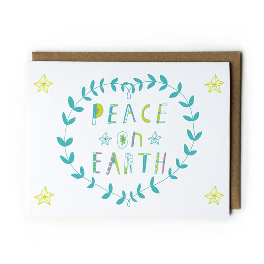 Holiday greeting card featuring hand-lettered "Peace on Earth" text in colorful teal and yellow, surrounded by a wreath-like leaf design and yellow stars, paired with a kraft paper envelope