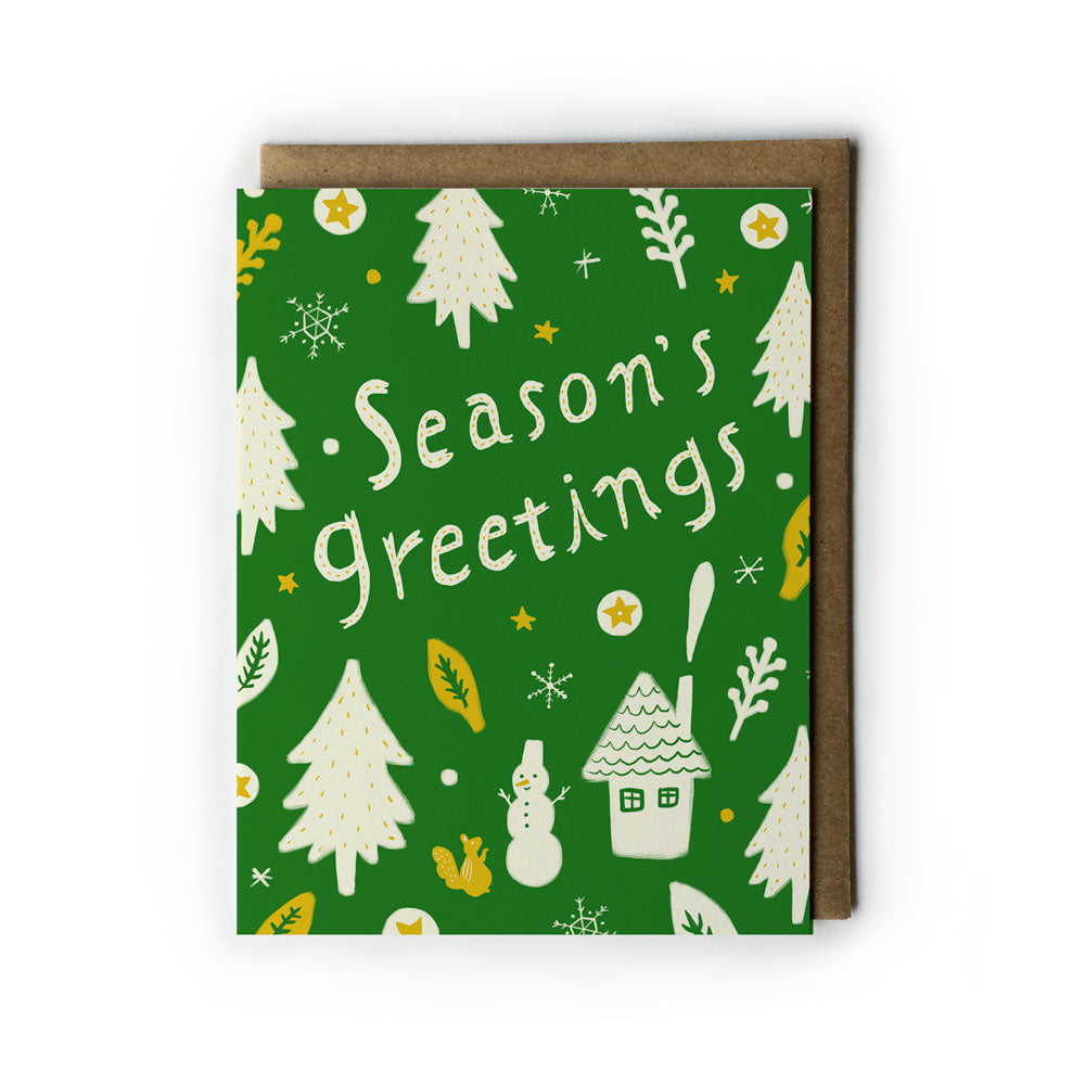 Season's Greetings holiday card with green background featuring white pine trees, snowflakes, snowman, house, and squirrel illustrations. Text reads "Season's Greetings" in white handwritten style. Kraft paper envelope included.