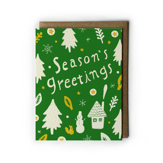 Season's Greetings holiday card with green background featuring white pine trees, snowflakes, snowman, house, and squirrel illustrations. Text reads "Season's Greetings" in white handwritten style. Kraft paper envelope included.