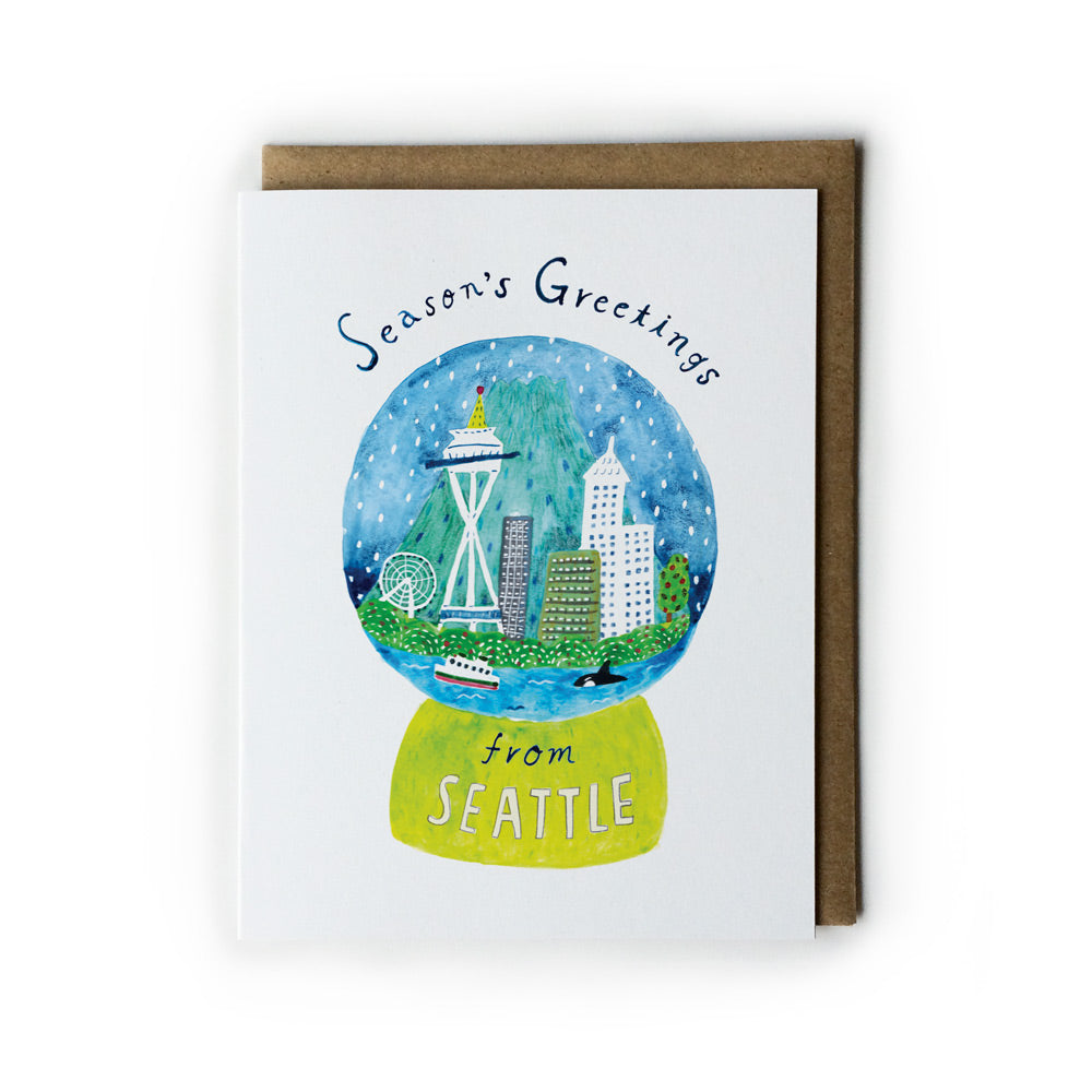 Watercolor greeting card featuring a Seattle snow globe with Space Needle, skyscrapers, and ferry boat. Text reads "Season's Greetings from Seattle" on a white card with brown envelope.
