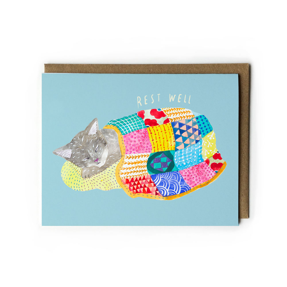 Greeting card featuring a sleeping gray cat wrapped in a colorful patchwork quilt, with "Rest Well" text above, on a light blue background, accompanied by a kraft paper envelope