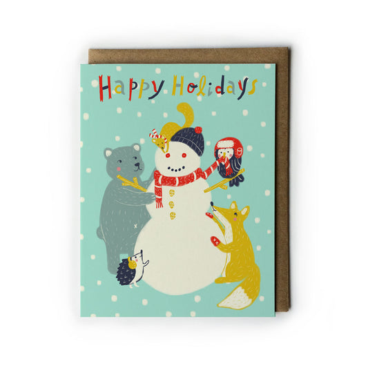 Cute holiday greeting card featuring a snowman with animal friends - bear, fox, owl, and mouse - on a snowy mint green background. Text reads "Happy Holidays" in colorful letters. Comes with kraft paper envelope.