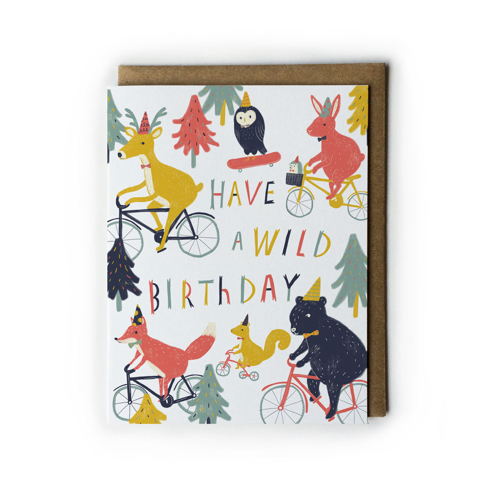 Colorful birthday card featuring whimsical animals on bicycles, including a deer, fox, and bear, with playful trees and text "HAVE A WILD BIRTHDAY" in vibrant lettering, accompanied by a kraft envelope.