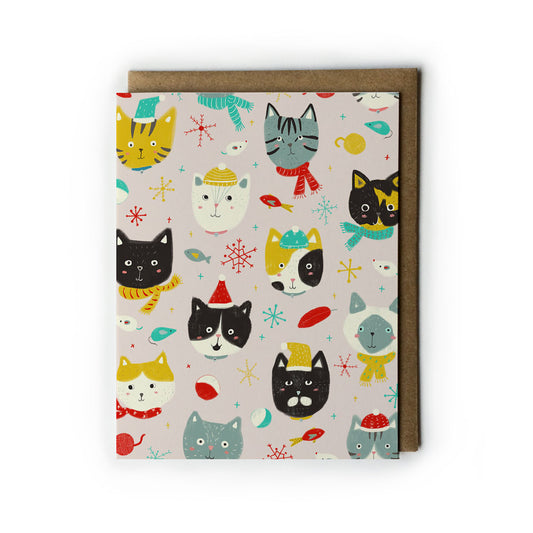 Festive greeting card featuring colorful cartoon cat faces with winter accessories like scarves and hats, surrounded by snowflakes and holiday decorations on a light background, paired with a kraft paper envelope