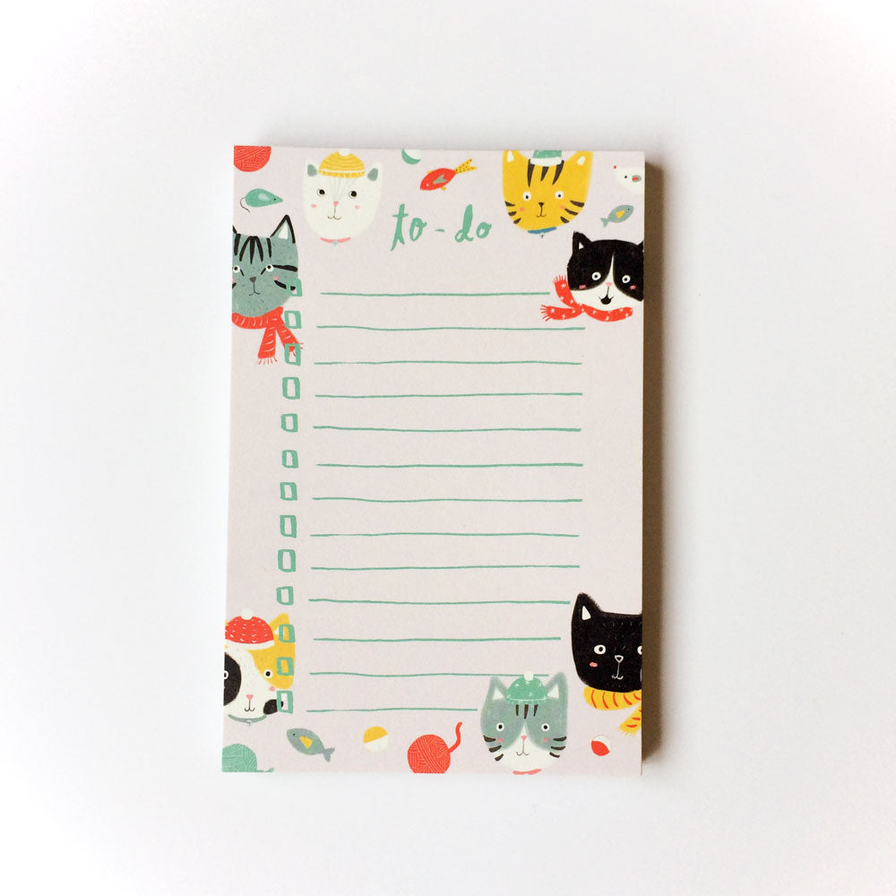 Cute winter-themed to-do list notepad with cartoon cat illustrations wearing scarves and hats, surrounded by colorful leaves and snowflakes, featuring blank lines for tasks