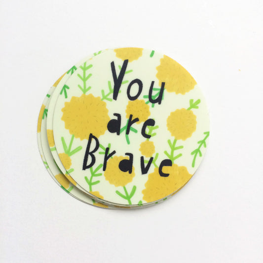 Circular vinyl sticker with "You are Brave" text in black, surrounded by yellow floral designs and green leaf patterns on a white background, measuring 3 inches in diameter