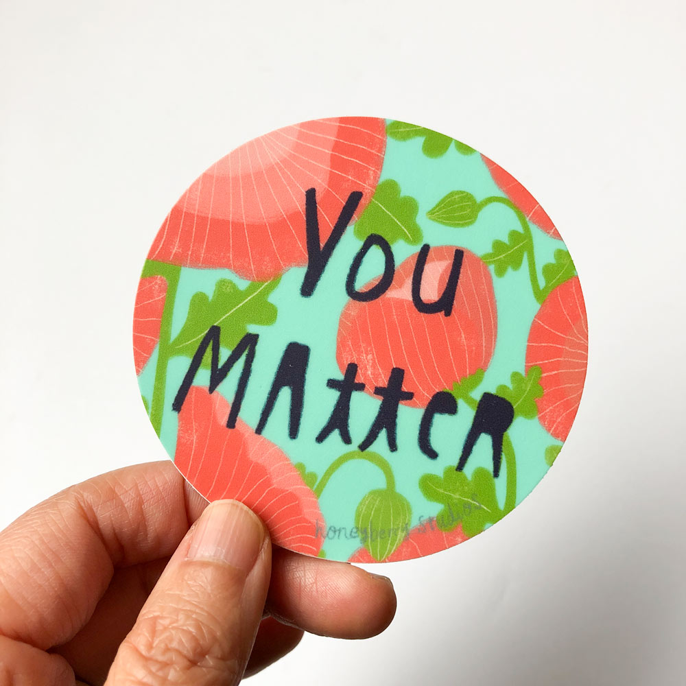 Colorful round vinyl sticker with "You Matter" text, featuring coral and teal background with green leaf designs, held by a hand showcasing its size and material quality