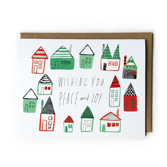 Whimsical watercolor holiday card featuring colorful folk-style houses with handwritten text "Wishing You Peace and Joy" in green and red tones, paired with a kraft paper envelope