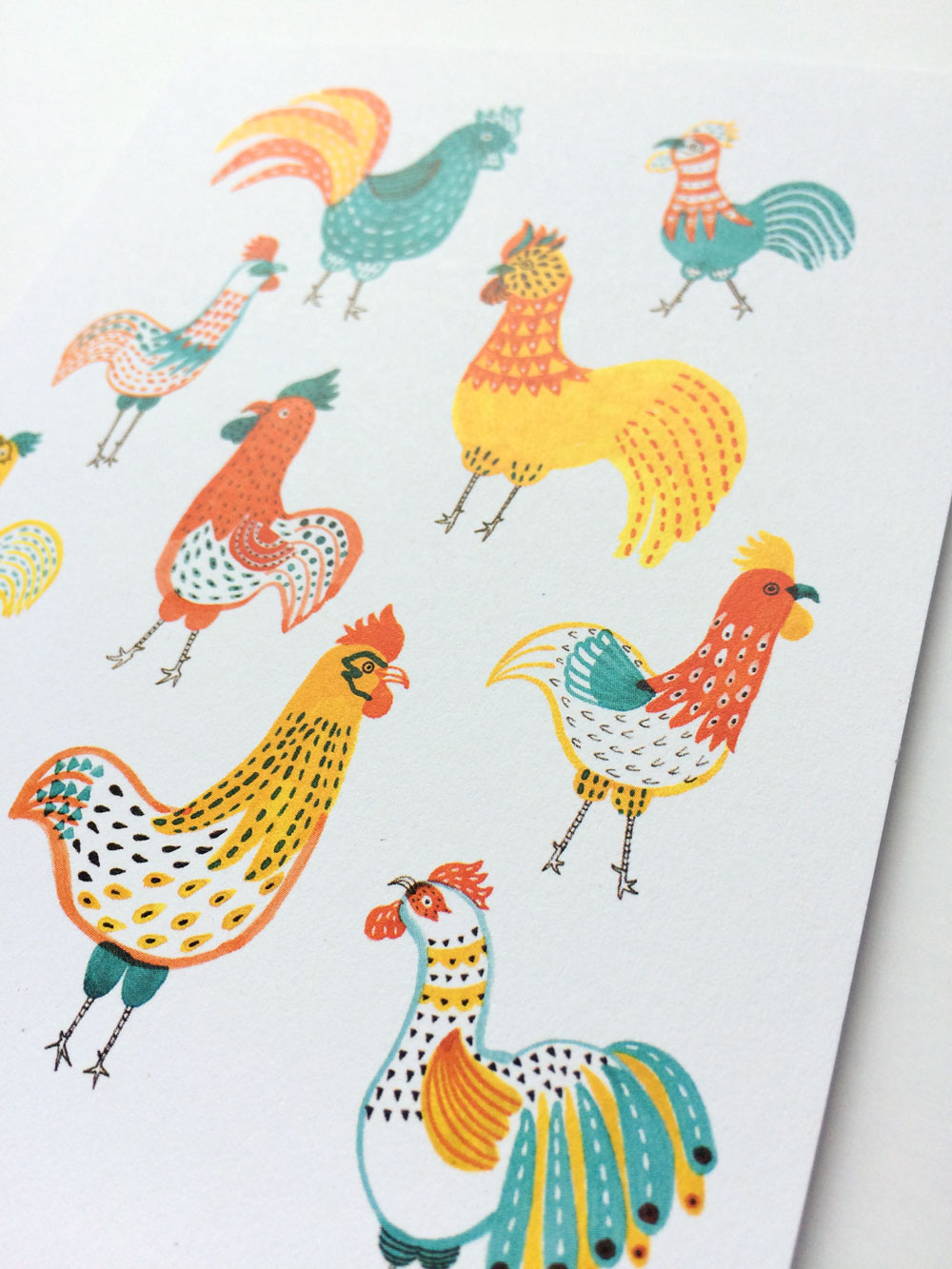 Colorful illustration of various rooster and chicken designs in vibrant patterns and hues, including teal, orange, yellow, and red, arranged on a white background, showcasing whimsical and stylized bird characters with unique feather details and poses.