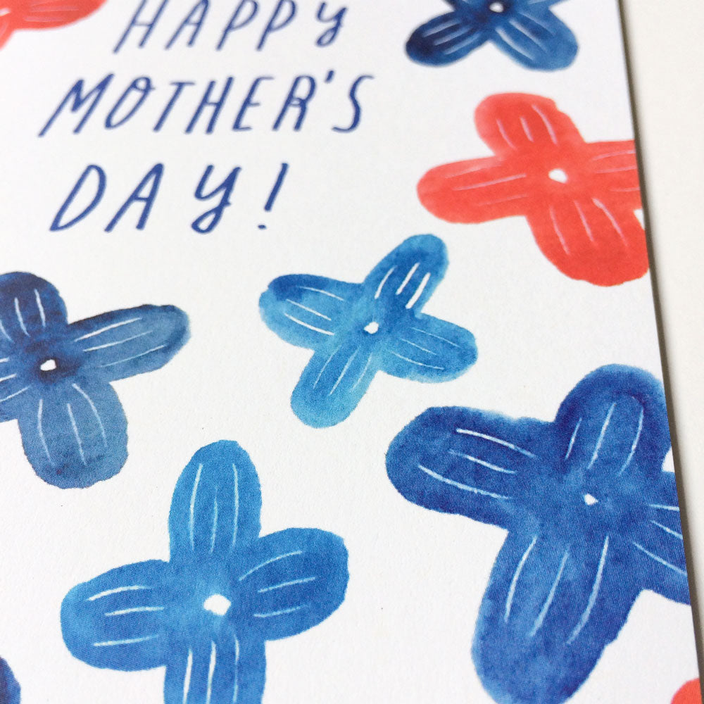 Blue and coral watercolor floral Mother's Day card with hand-lettered text, featuring stylized lilac blooms on white recycled cardstock, offering a unique and eco-friendly alternative to traditional pink and red designs