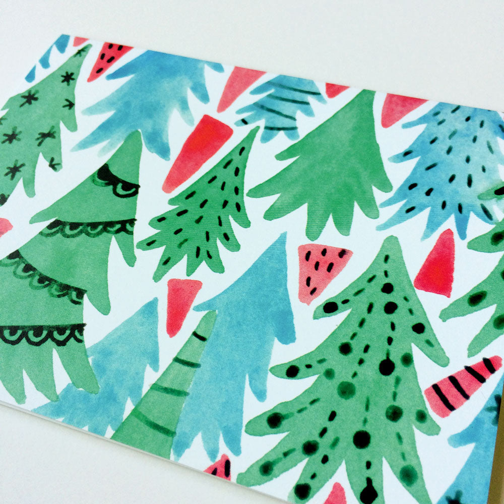 Whimsical watercolor greeting card featuring stylized Christmas trees in green and blue with red accents, creating a festive forest pattern on white background