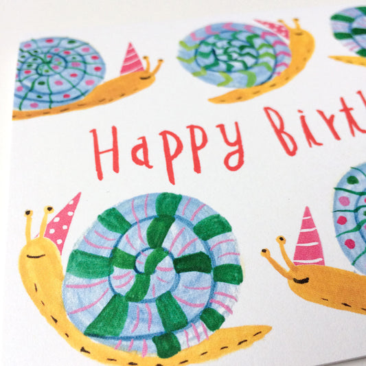 Colorful birthday card featuring whimsical cartoon snails with patterned shells wearing party hats, surrounding text reading "Happy Birth". Close-up view showing vibrant watercolor-style illustration on white background.