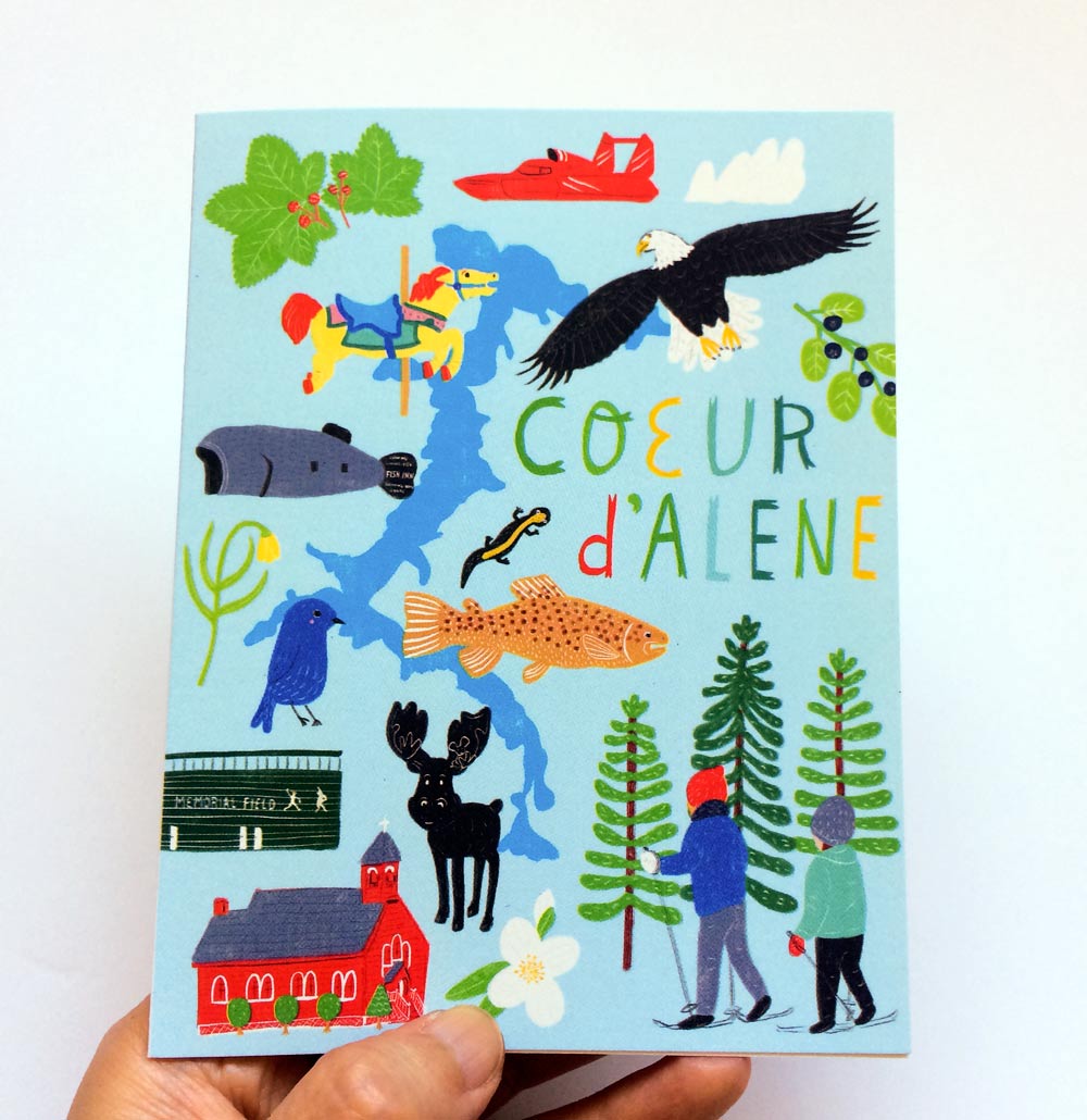Colorful illustrated greeting card featuring Coeur d'Alene landmarks, wildlife, and activities including a lake, eagle, fish, deer, hikers, pine trees, and a red barn, with hand-lettered text "COEUR d'ALENE" in vibrant colors