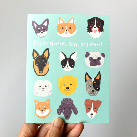 Dog Mom Mother's Day card featuring colorful illustrations of diverse dog breeds' faces on a mint green background, held by a hand. Text reads "Happy Mother's Day, Dog Mom!