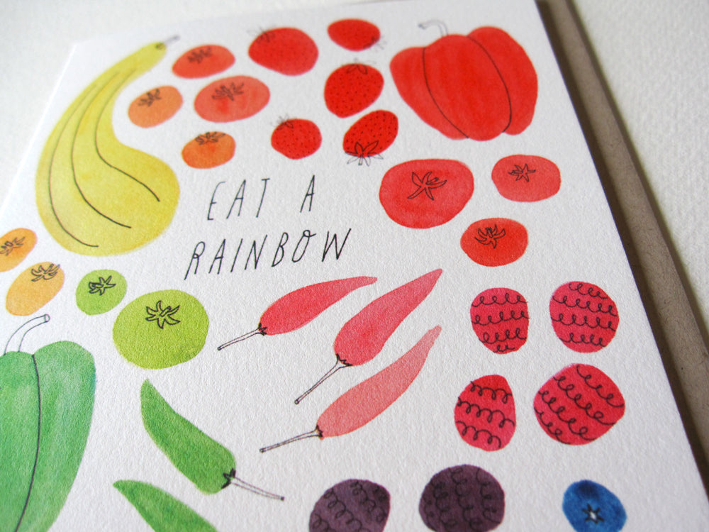 Colorful watercolor illustration of various fruits and vegetables arranged in a rainbow pattern with text "Eat a Rainbow" in the center, showcasing diverse produce in red, orange, yellow, green, and blue hues.