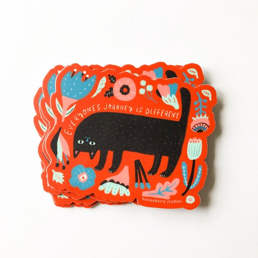 Colorful vinyl sticker featuring a black cat silhouette surrounded by floral and nature elements on a vibrant orange background with the text "Everyone's Journey is Different