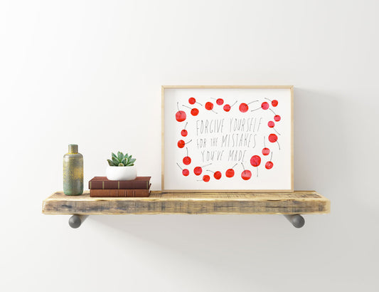 Framed art print with handwritten text "Forgive yourself" surrounded by red watercolor cherries, displayed on rustic wooden shelf with books, plant, and vintage bottle