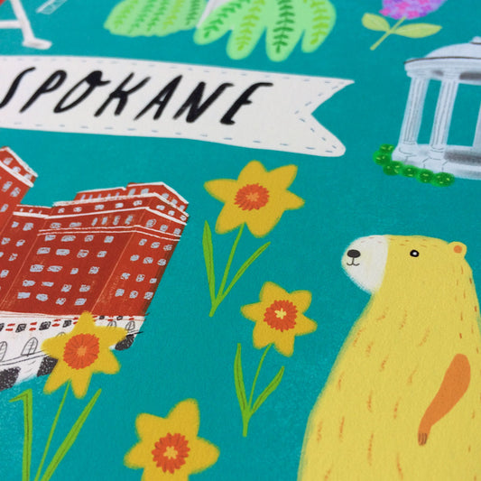 Colorful illustration featuring Spokane landmarks and symbols including a red brick building, yellow flowers, and a cartoon marmot on a teal background with a white banner reading "Spokane