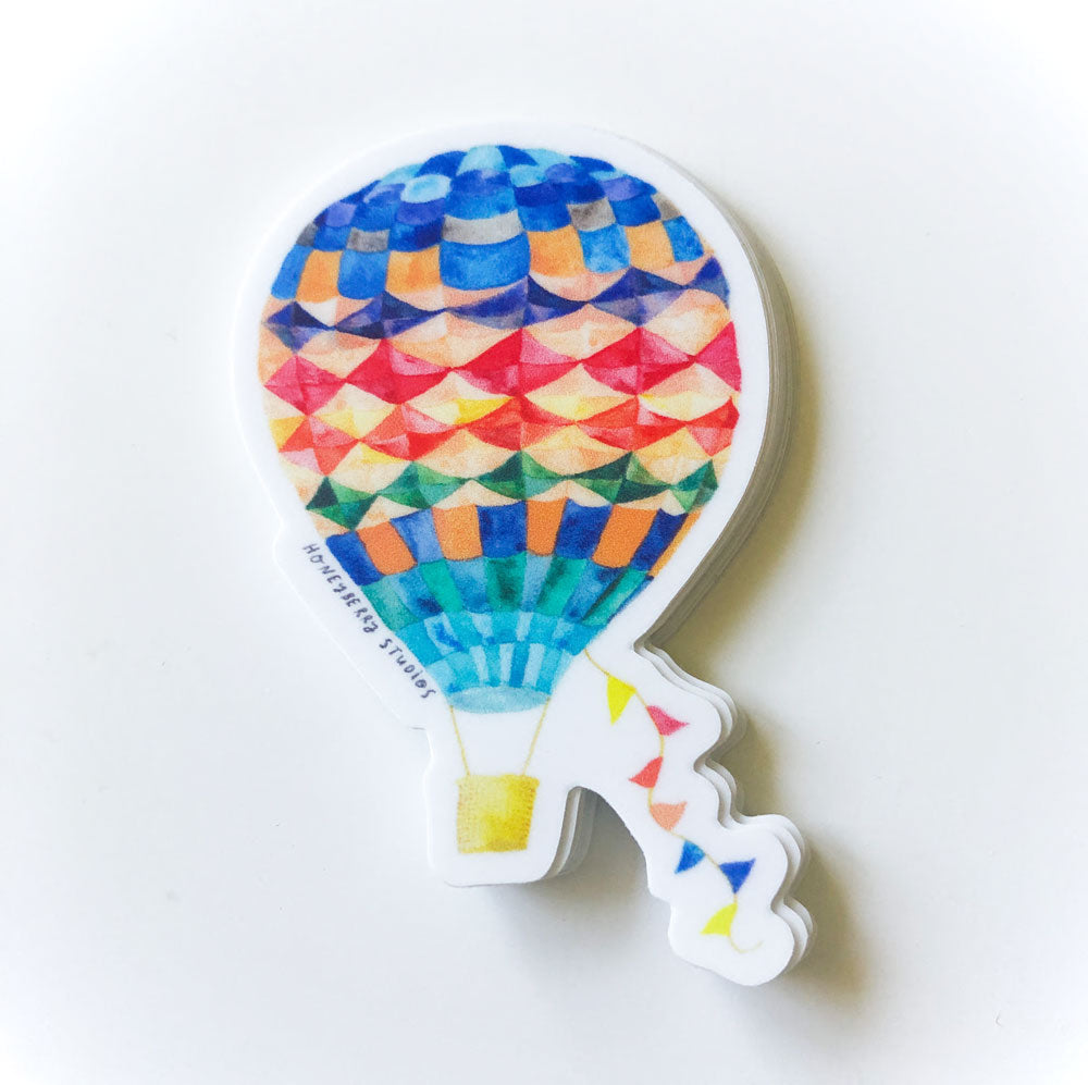 Colorful hot air balloon vinyl sticker with geometric pattern design, featuring vibrant blue, red, orange, and green hues, accompanied by small multicolored triangular flags trailing behind
