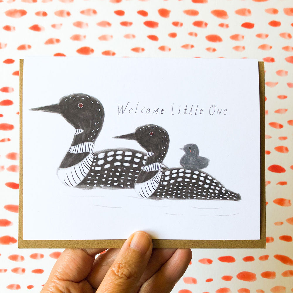 Loon family greeting card with "Welcome Little One" message, featuring hand-drawn black and white illustrations of adult loons with a baby, displayed on colorful spotted background