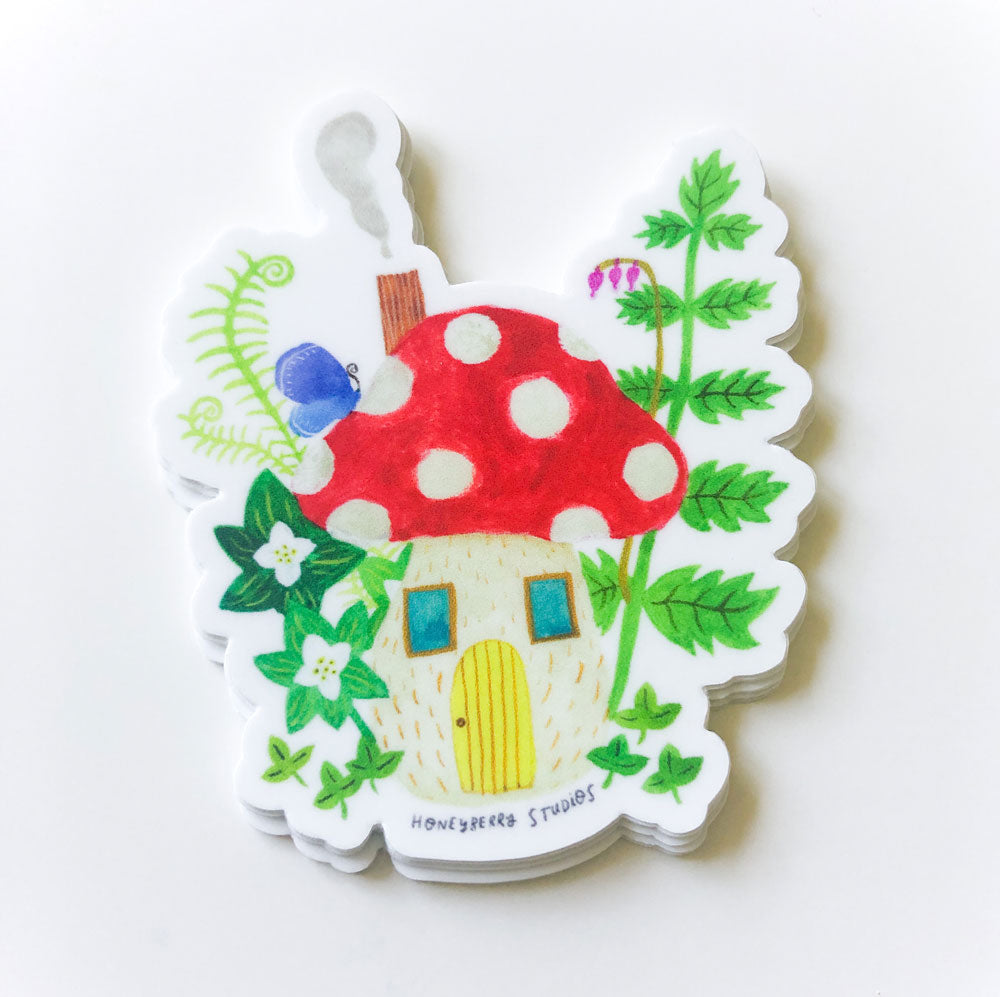 Whimsical vinyl sticker featuring a colorful mushroom house with red polka dot cap, yellow door, surrounded by green foliage and flowers, perfect for indoor or outdoor decoration