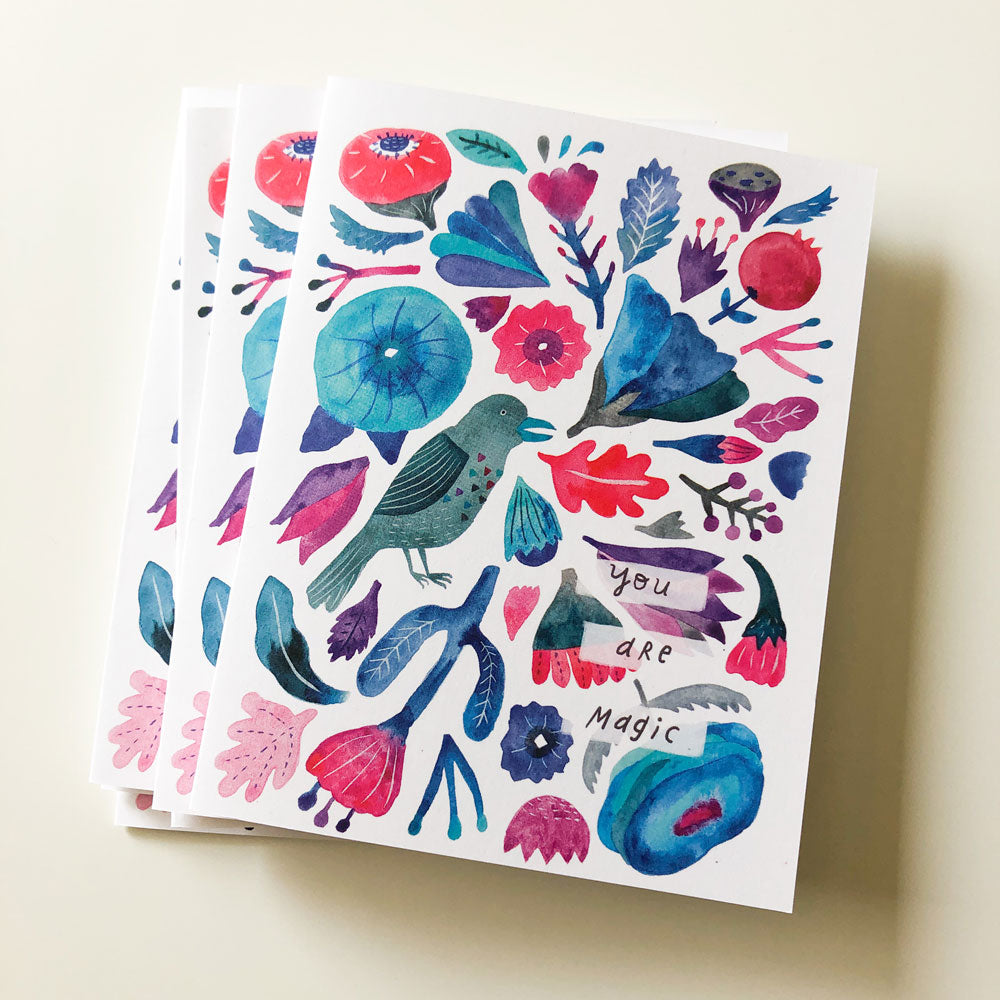 Colorful greeting card with whimsical watercolor illustrations of flowers, leaves, and a raven, featuring the text "You are magic" on a white background. Vibrant hues of blue, red, and teal create a lively and enchanting design perfect for special occasions.