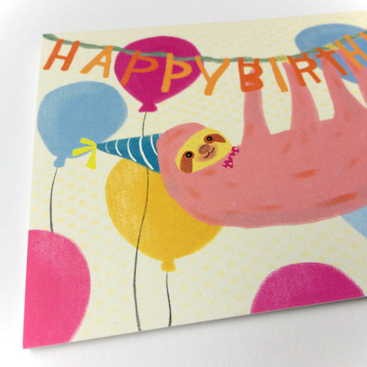 Cute pink sloth wearing party hat, hanging from 'Happy Birthday' banner with colorful balloons on cream background, perfect for festive birthday greeting card
