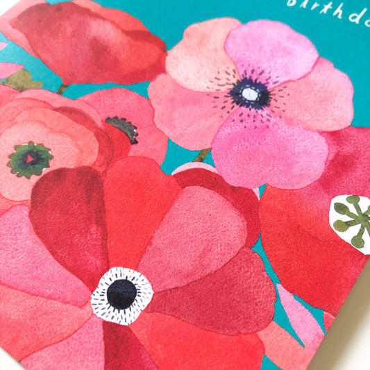 Vibrant watercolor poppy birthday card featuring large red and pink blossoms with dark centers on a teal background, showcasing delicate floral details and artistic brush strokes