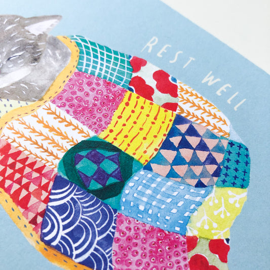 Colorful patchwork quilt with various patterns covering a sleeping cat, text "REST WELL" visible in corner, blue background, part of greeting card design for compassionate support