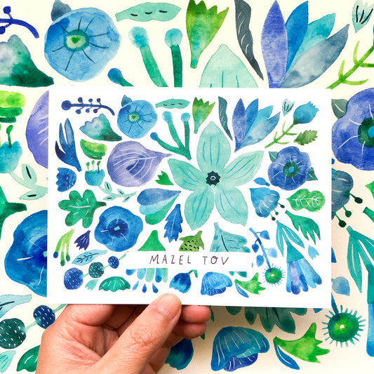 Watercolor greeting card with vibrant blue and green floral patterns, featuring various flower shapes and leaves. The words "Mazel Tov" are written in the center, and a hand is shown holding the card against a matching background.